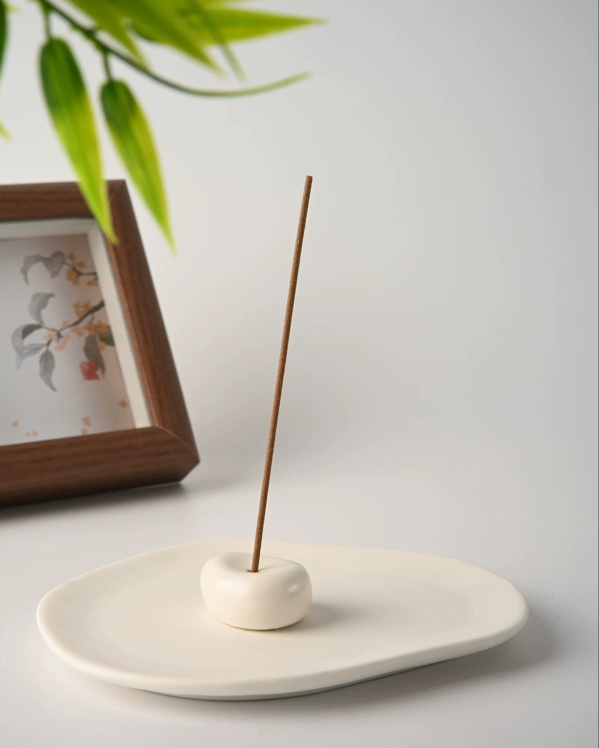 The stone holder centred on the ceramic tray with a lit incense stick, framed print in the background