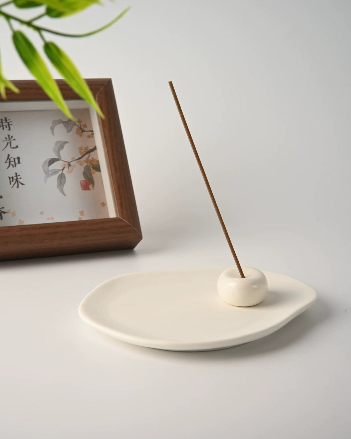 Ceramic incense tray with the stone holder set near one edge and a tall incense stick burning