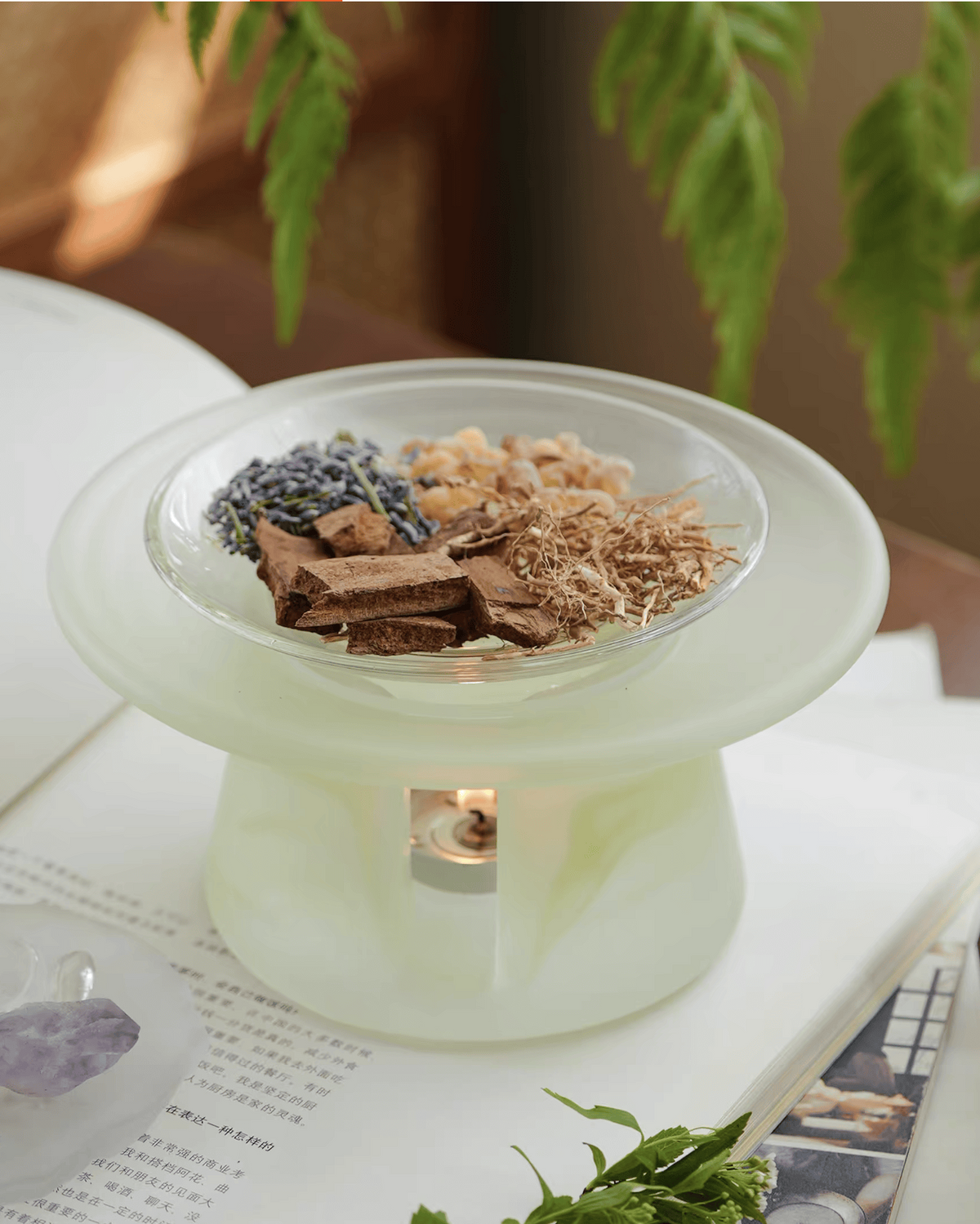 Celadon green glass incense warmer with bark, lavender and dried roots warming above a lit tealight