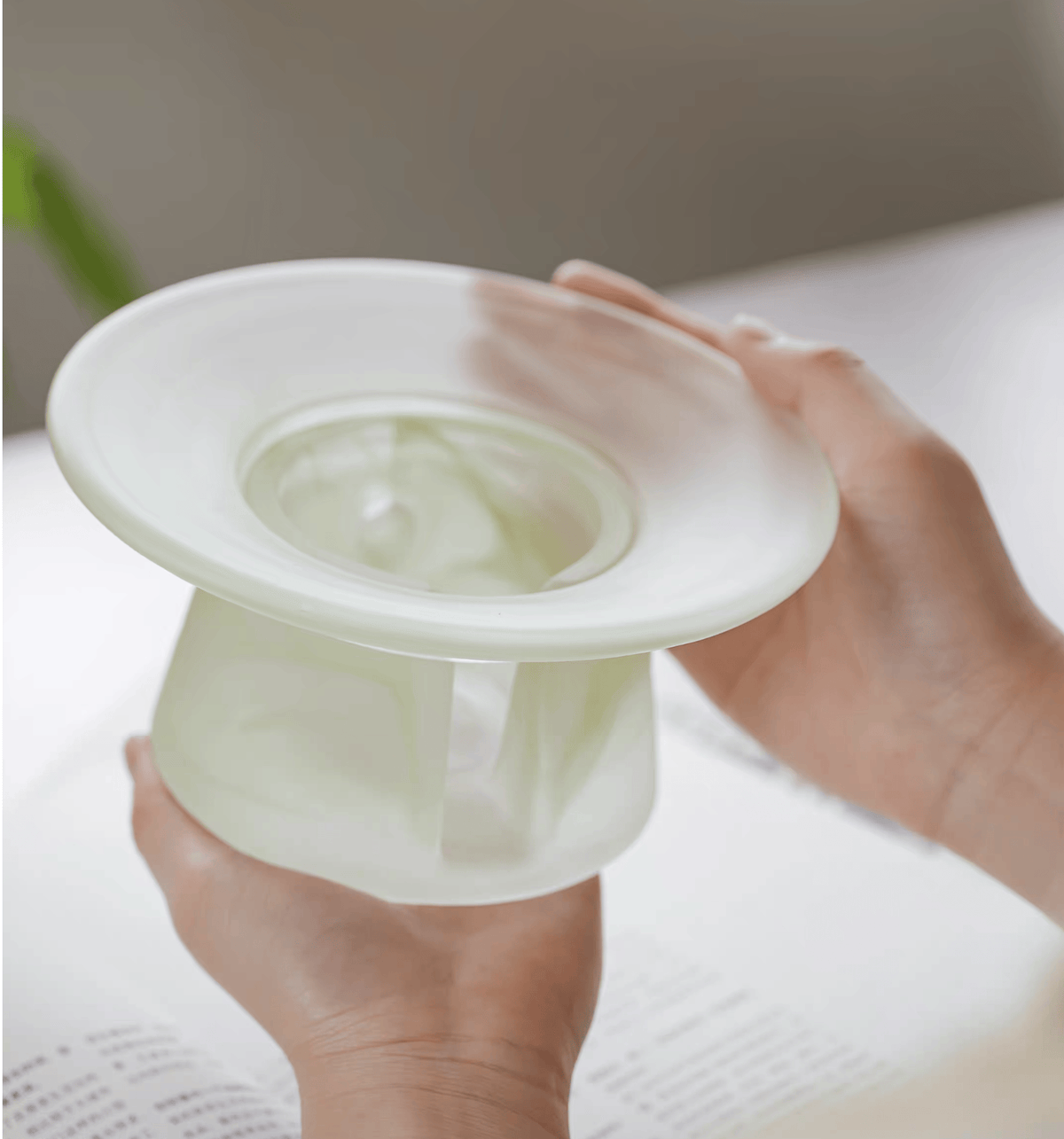 Hands holding a bone white liuli glass incense warmer, upper dish empty, showing the shape