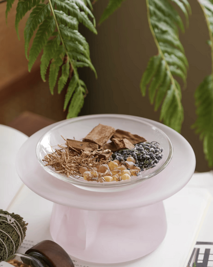 Blossom pink glass incense warmer holding bark pieces, dried roots and lavender buds in the dish