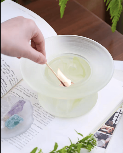 A hand lighting the tealight beneath a celadon green glass incense warmer