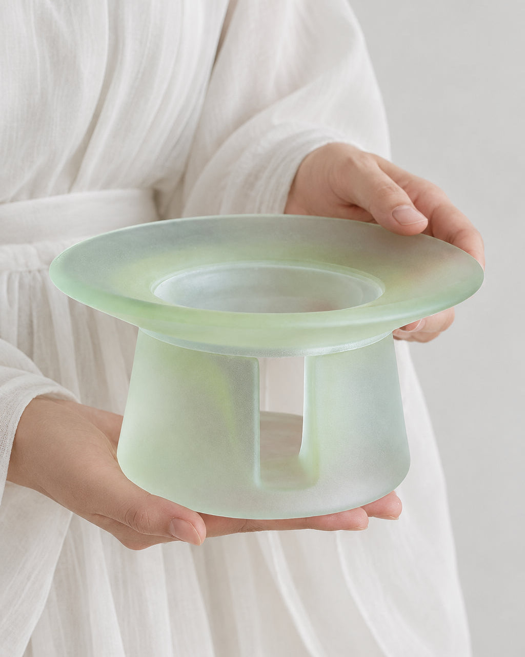 A person in white linen holding a celadon green liuli glass incense warmer