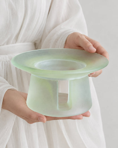 A person in white linen holding a celadon green liuli glass incense warmer