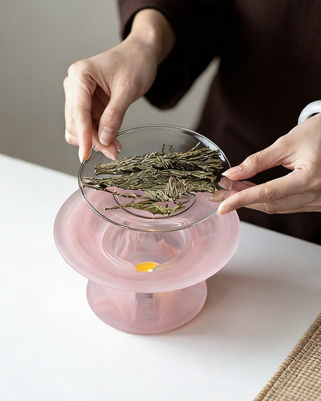 Two hands lifting the glass dish off a blossom pink incense warmer to show it is removable